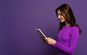 mulher com blusa roxa lendo um tablet
