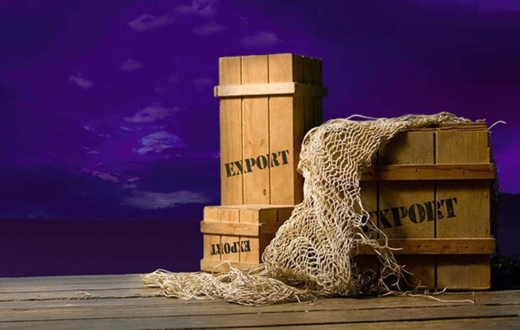 Fundo com céu roxo, e em um deck perto do mar, também roxo, temos caixas de madeira, representando a emissão de nota fiscal de exportação