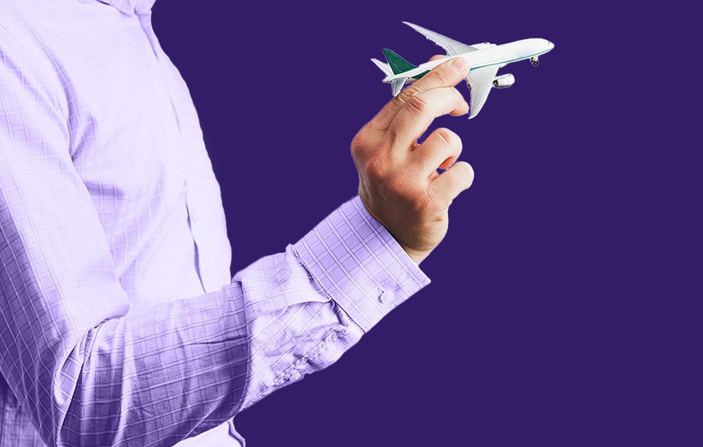 Na imagem, temos o torso de um homem, com camisa social, segurando avião em miniatura simulando um vôo, simbolizando o seguro de transporte de cargas.