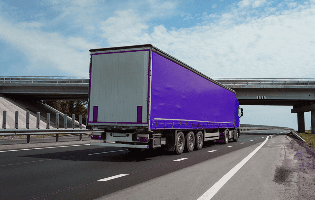 Caminhão com cores roxa e branca em rodovia simbolizando o modal de transporte.