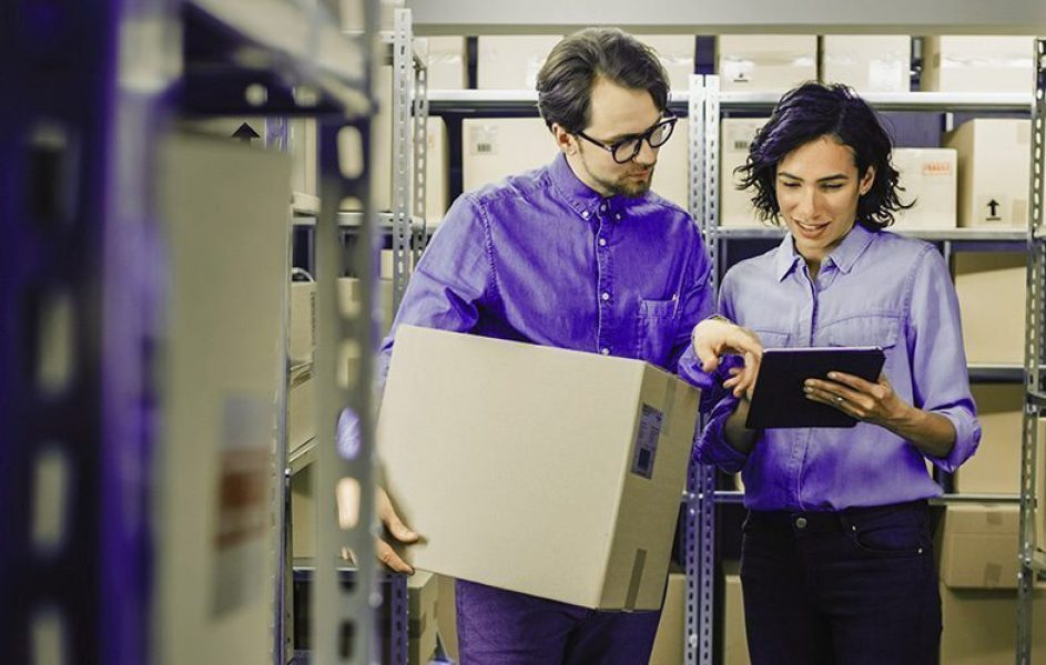 importação por remessa expressa Dois funcionários olhando para um tablet e com uma caixa de papelão na mão, simbolizando a Importação por Remessa Expressa.